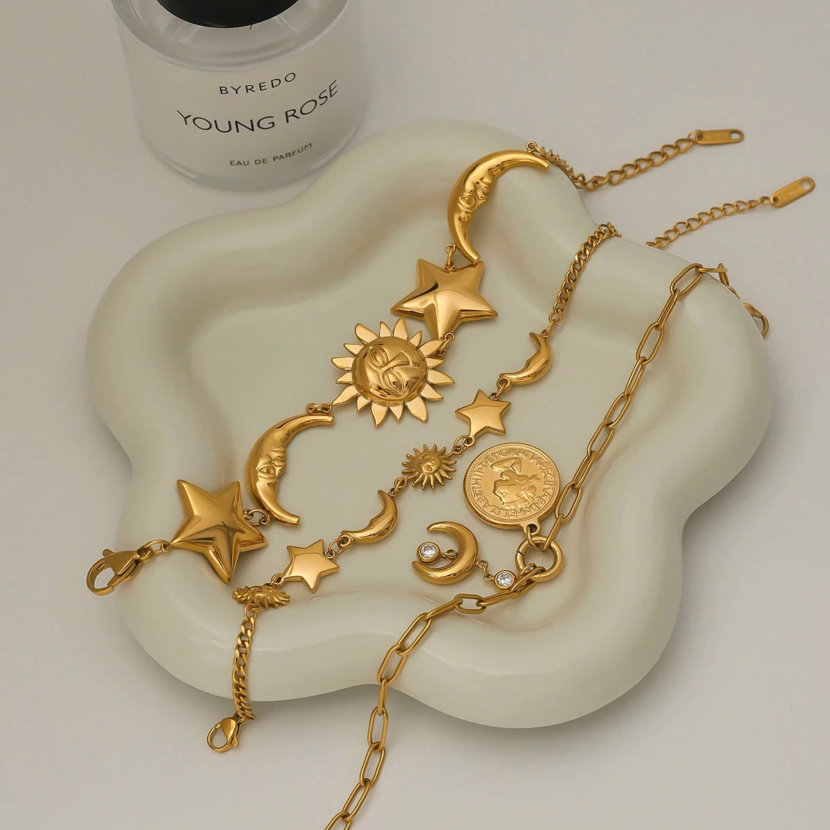 Gold celestial motif bracelet with sun, moon, and star charms on a white wavy dish