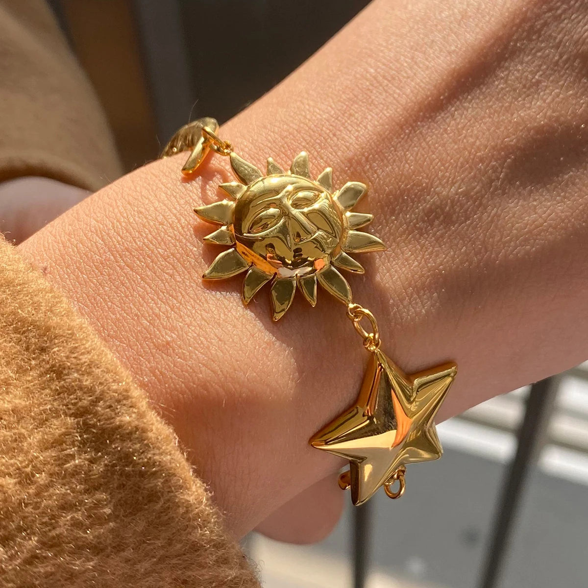 Gold celestial motif bracelet with sun and star charms worn on wrist in natural light