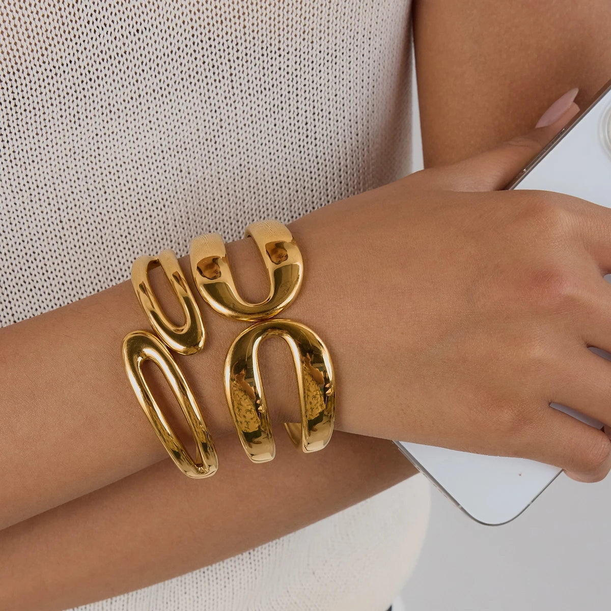 Close-up of a wrist with chunky everyday gold jewelry bracelets on a person holding a white phone