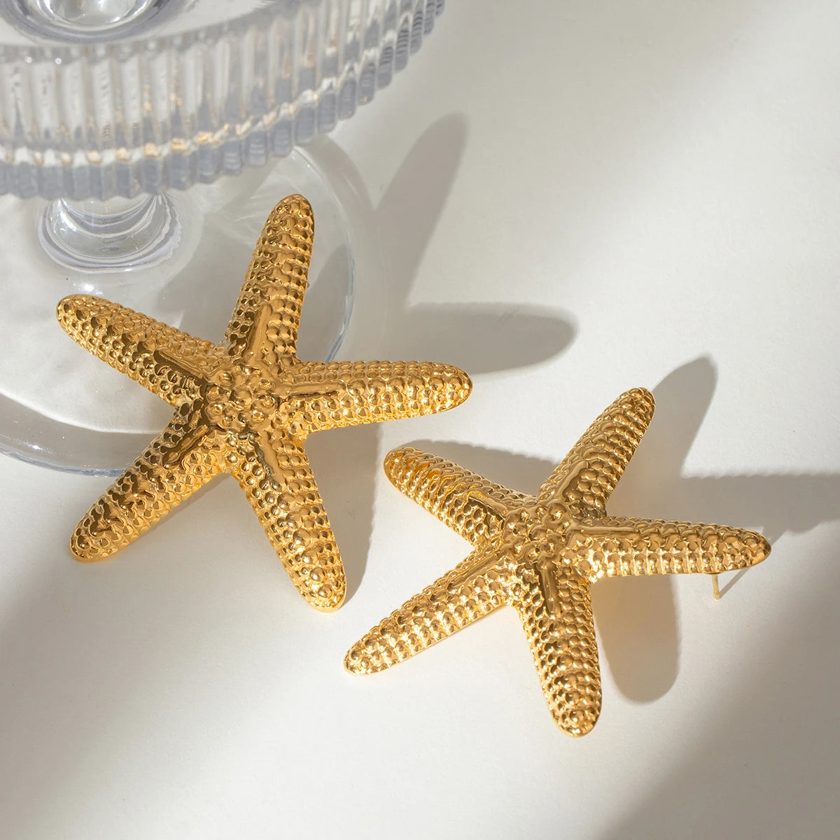 Gold plated earrings shaped like textured starfish with a shiny finish by A minha loja