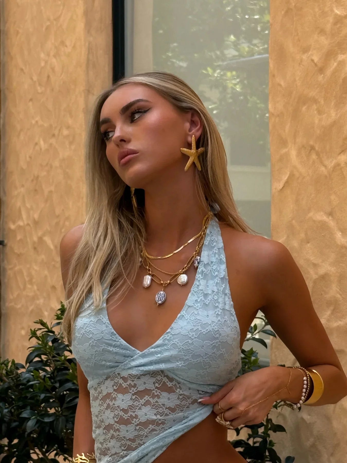 Woman wearing gold plated earrings shaped like starfish and layered gold necklaces in outdoor setting