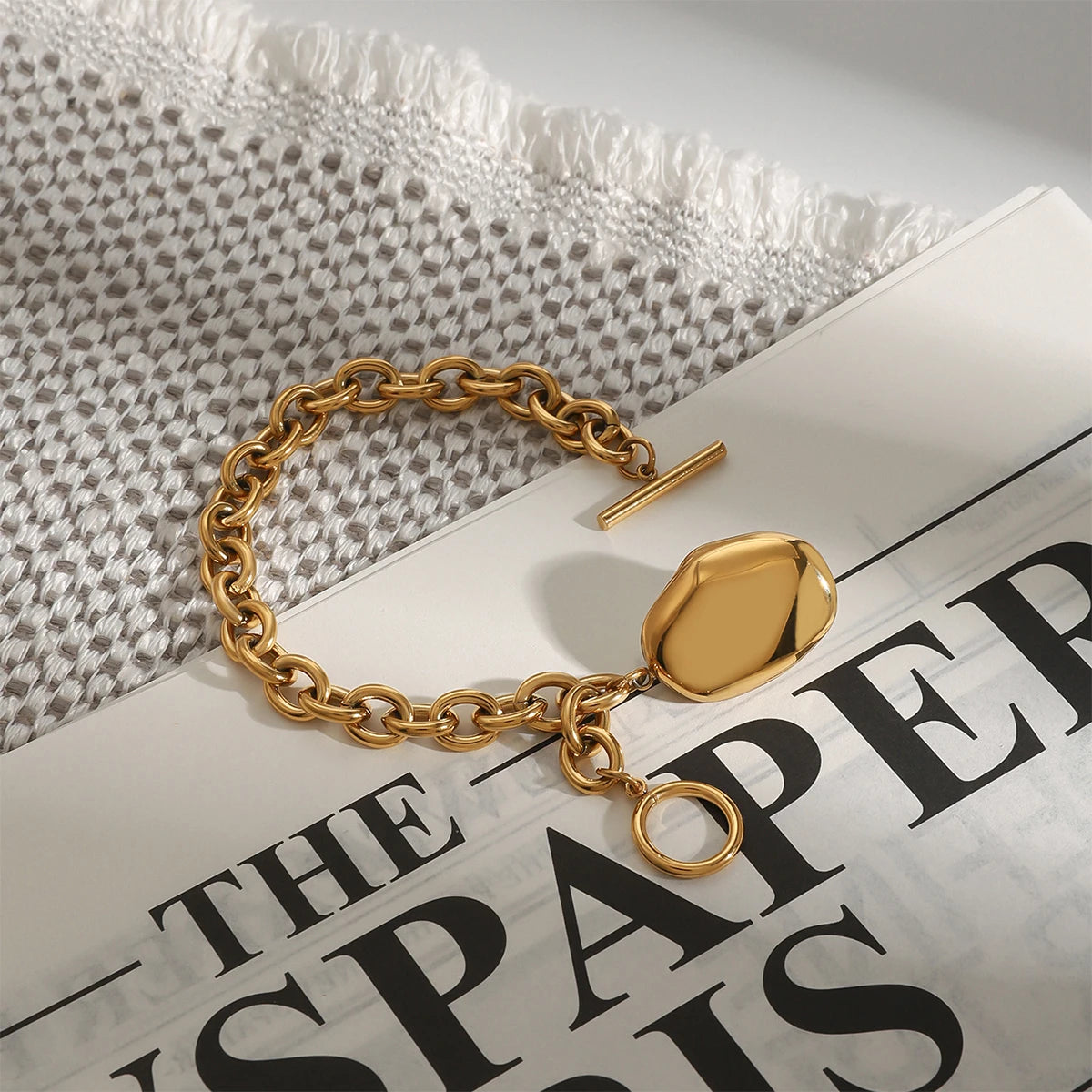 Gold tone stacked chain bracelet with large links and a toggle clasp on a newspaper background