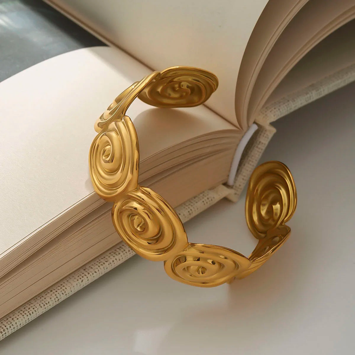 Close-up of adjustable gold bracelet with spiral patterns placed on an open book