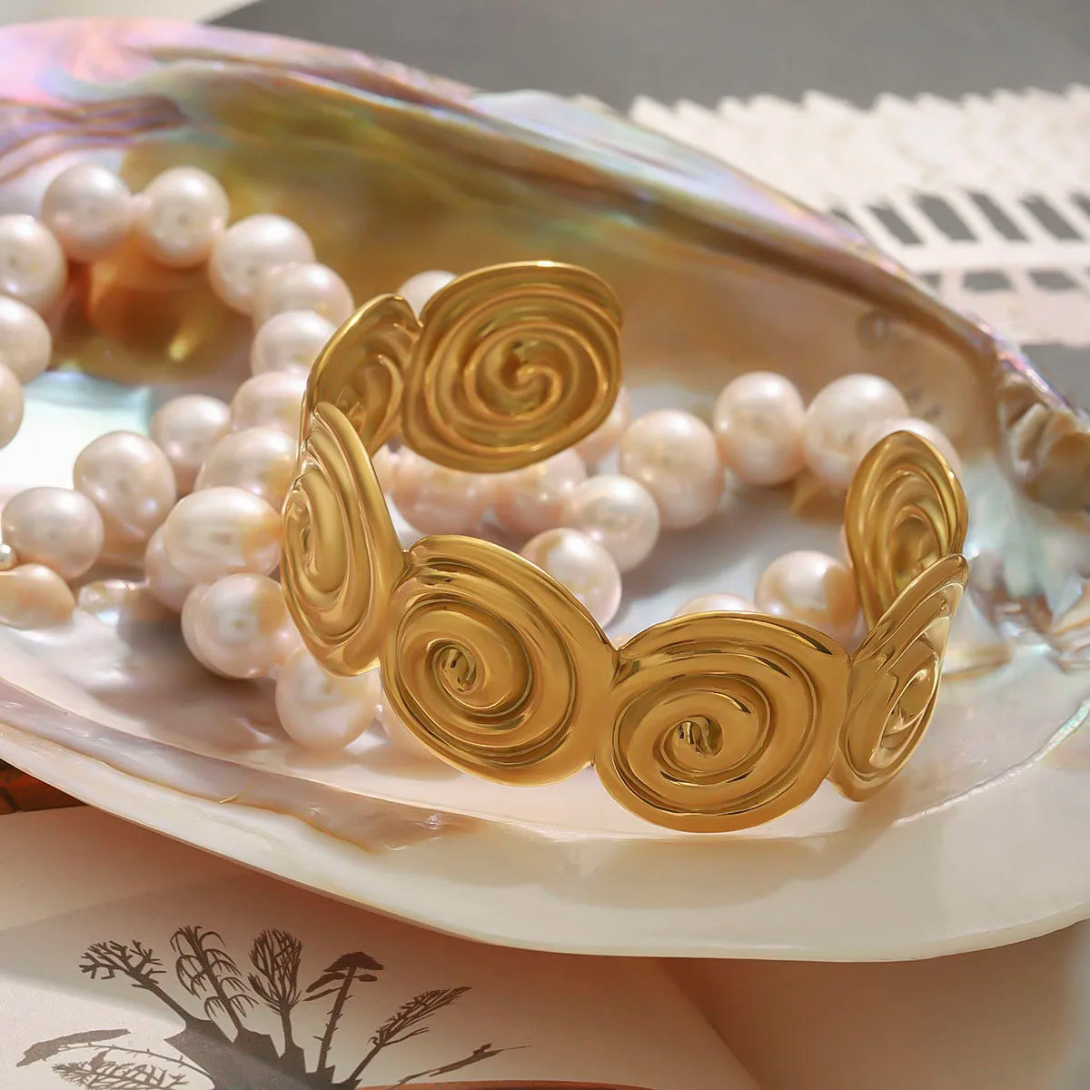 Adjustable gold bracelet with spiral design displayed on a shell next to a pearl necklace