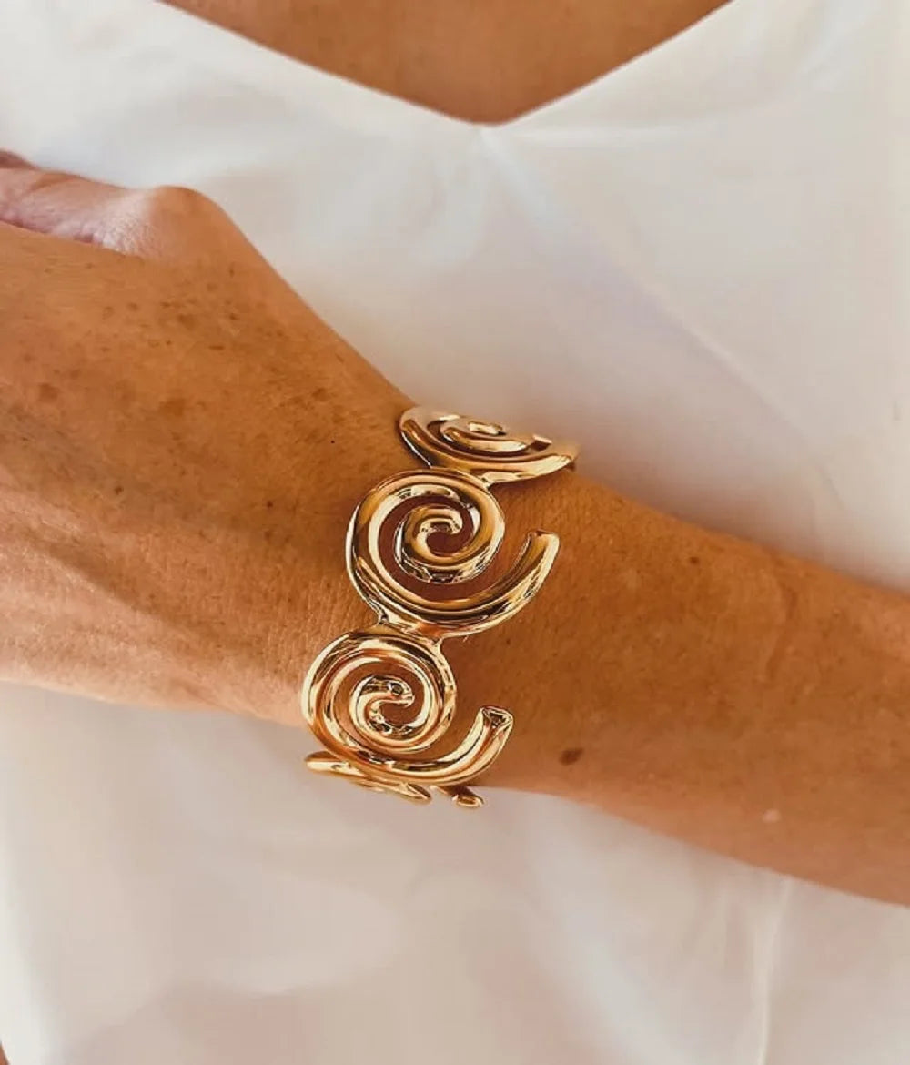 Elegant adjustable gold bracelet with swirling design worn on wrist with white top background