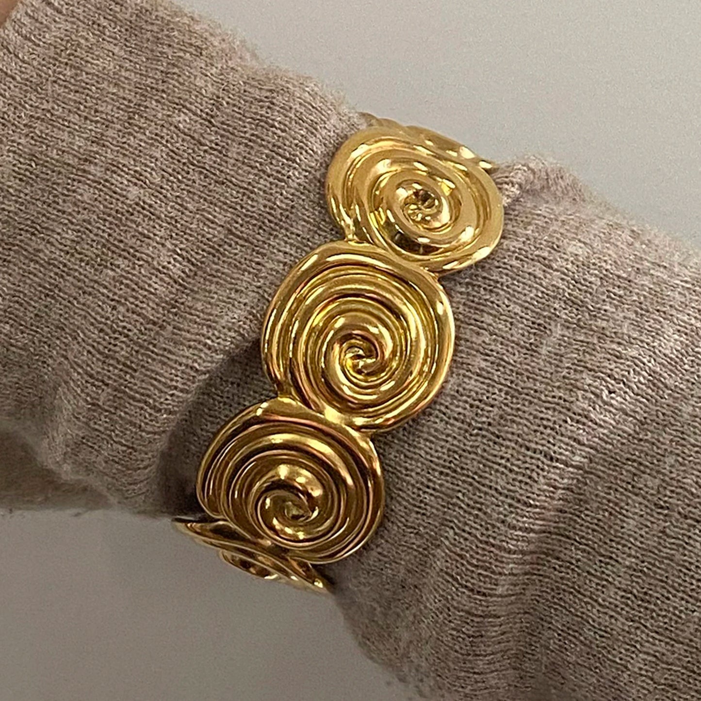Adjustable gold bracelet featuring spiral design worn on wrist over beige knit fabric