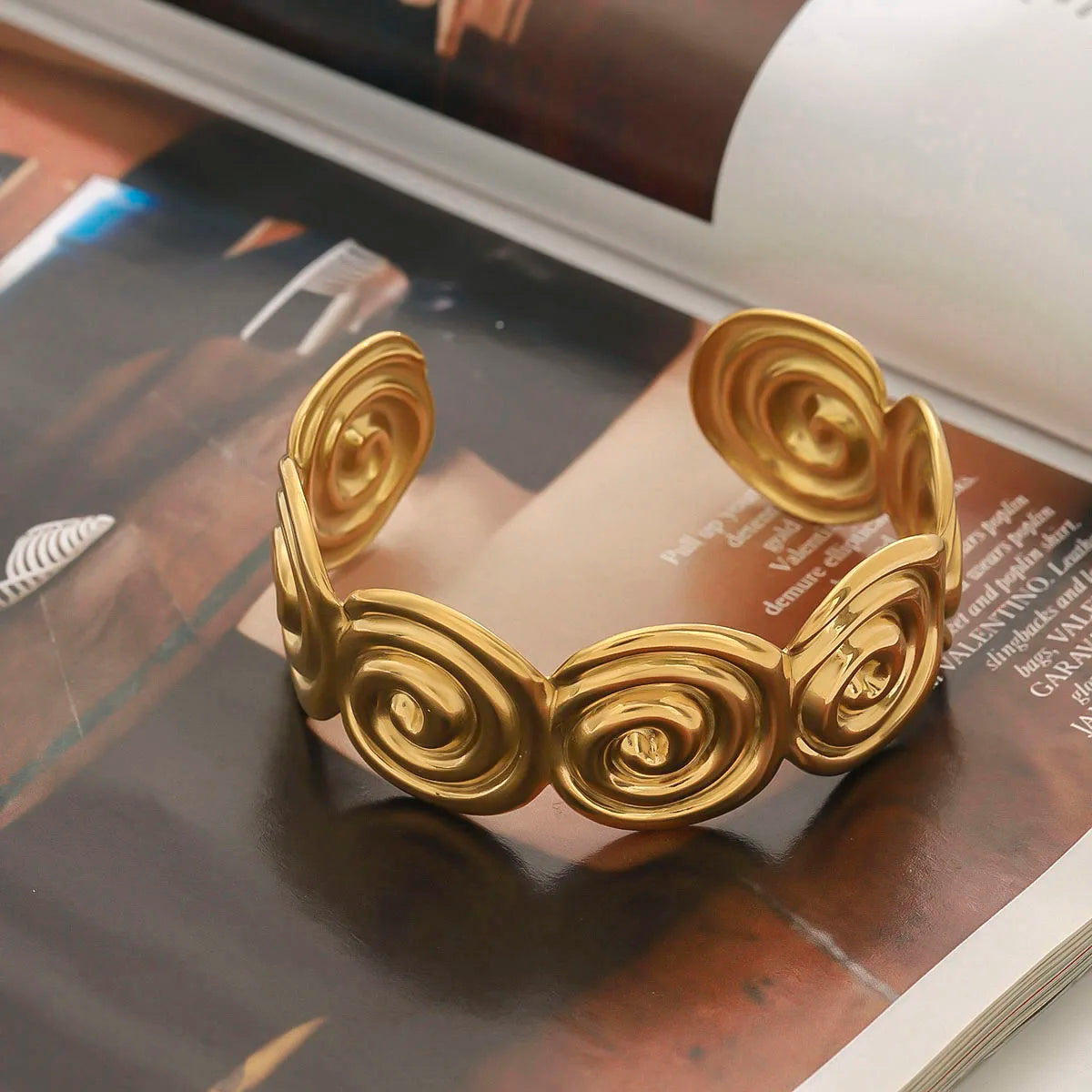 Adjustable gold bracelet with a spiral design displayed on an open magazine page