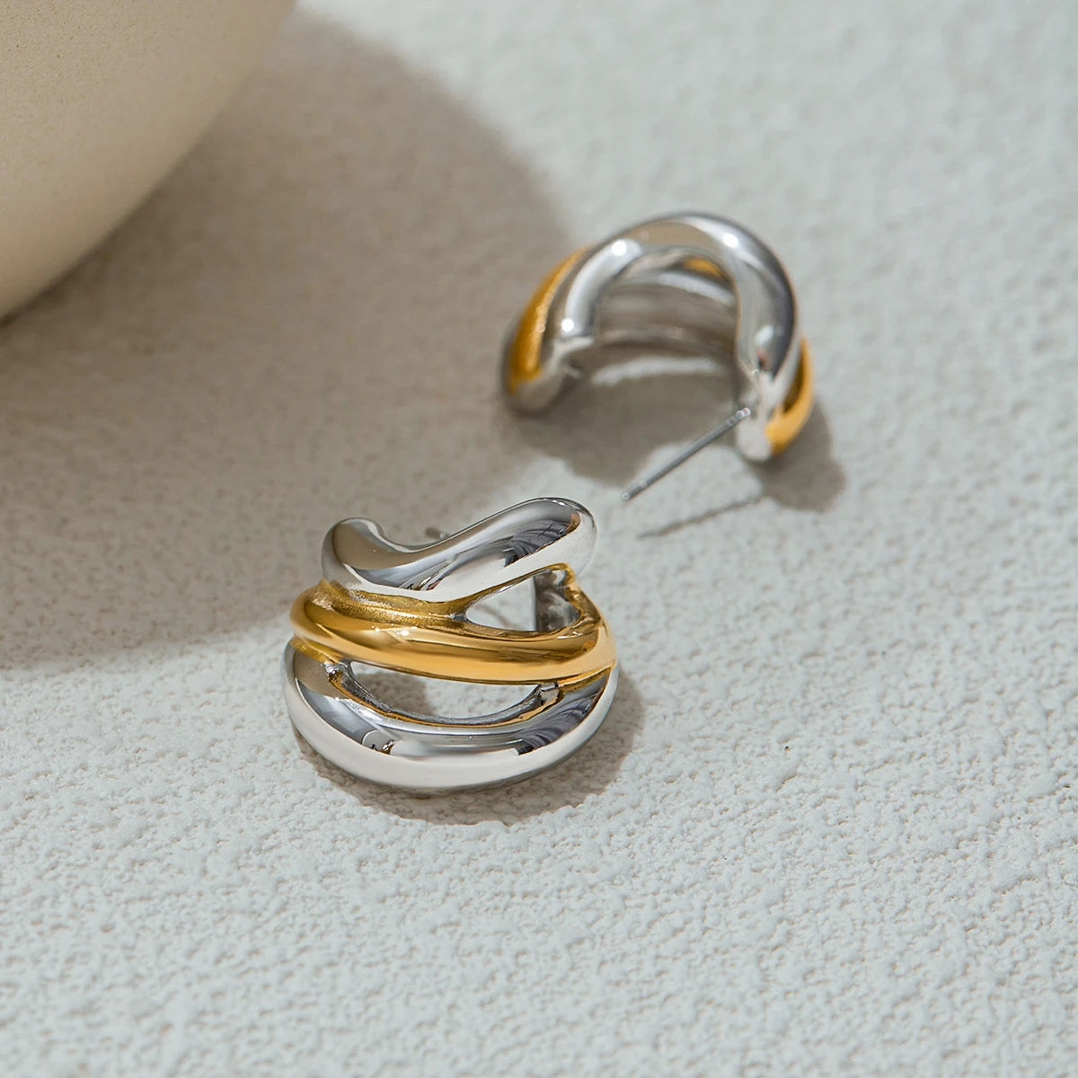 Silver and gold twisted luxury stud earrings on textured surface by A minha loja