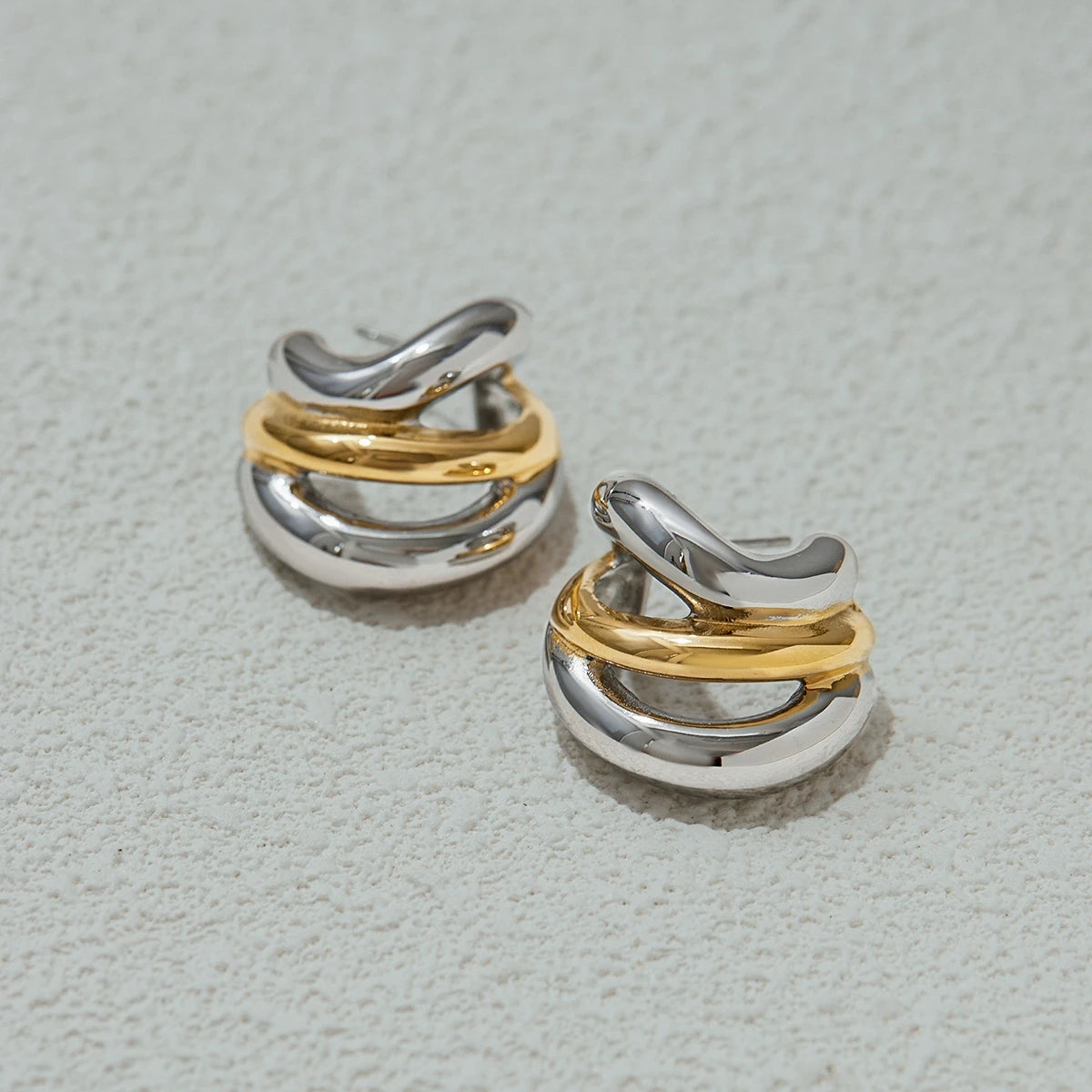 Two-tone gold and silver luxury stud earrings with a twisted design on textured surface