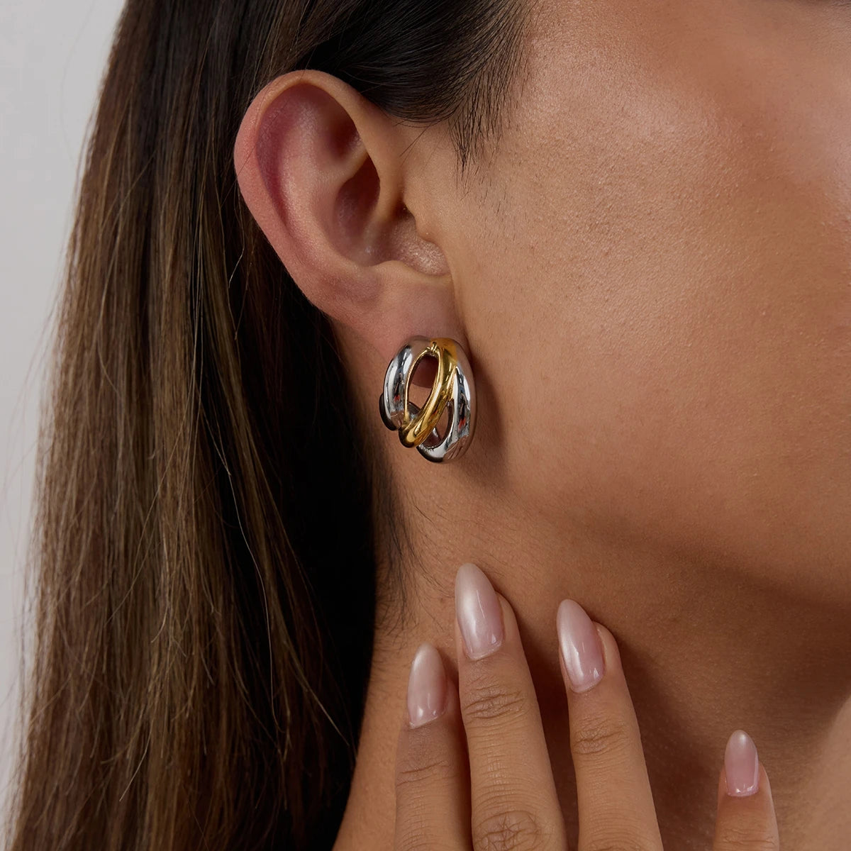 Close-up of ear wearing luxury stud earrings with intertwined gold and silver hoops