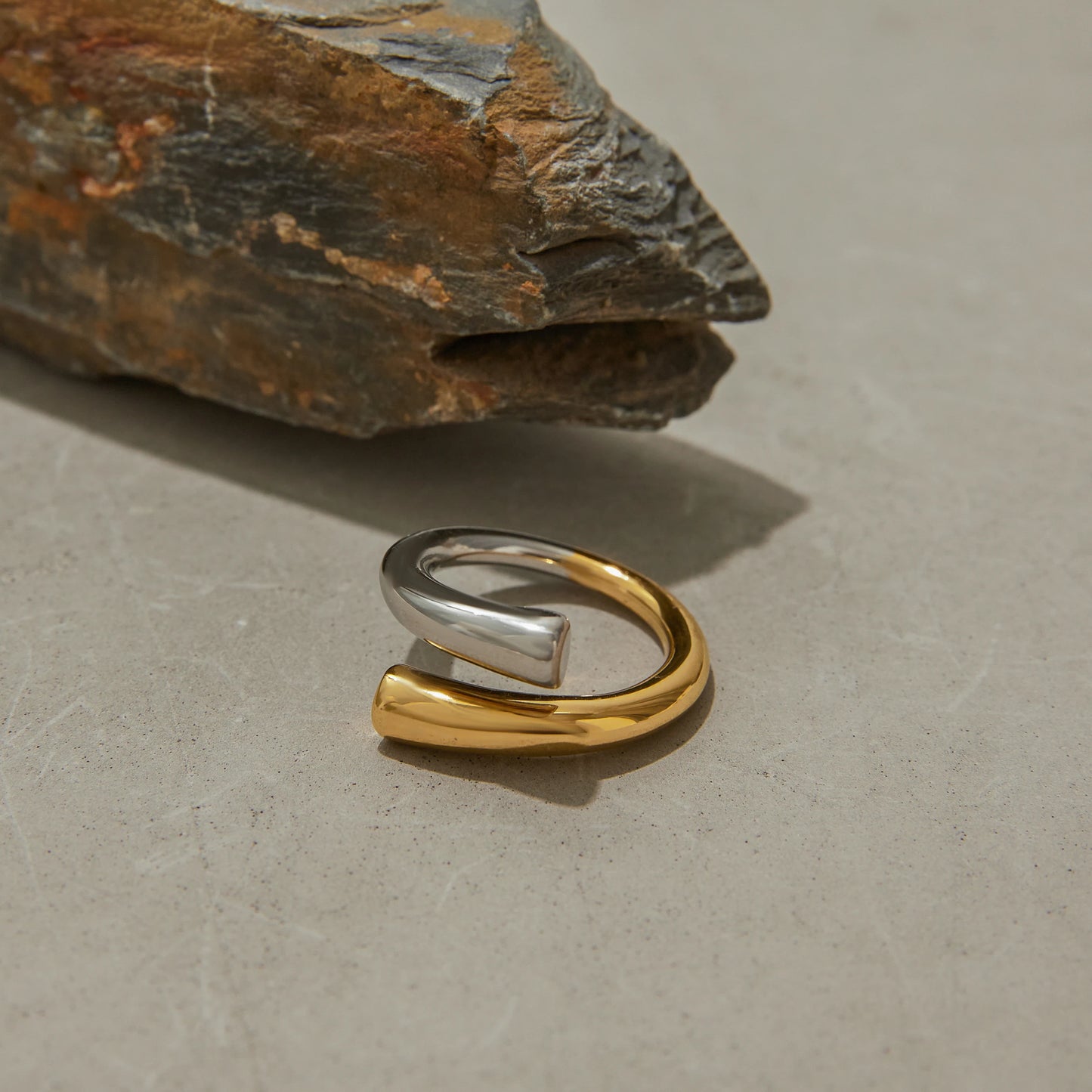 Two-tone stainless steel line ring with silver and gold finish displayed on a stone surface