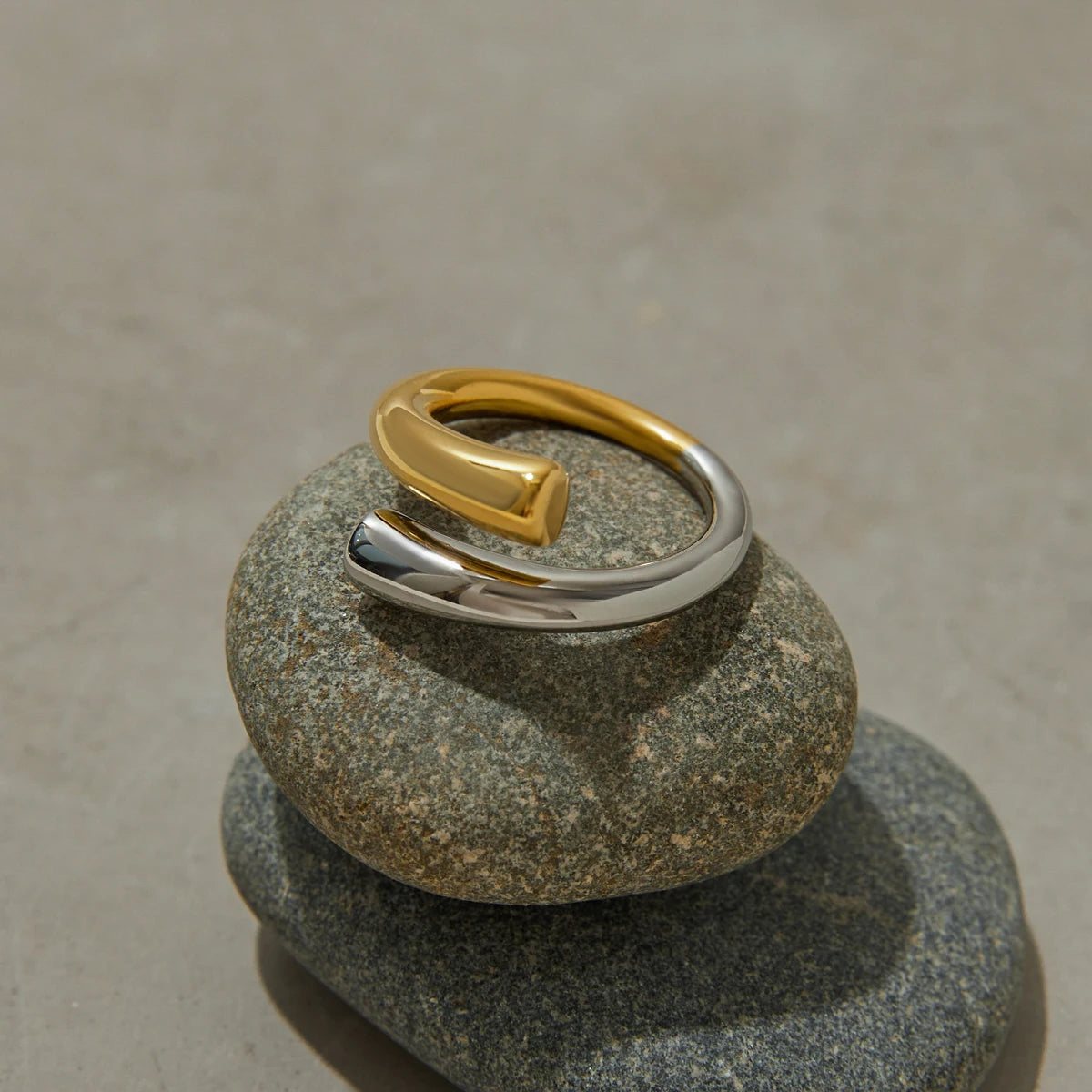 Two-tone stainless steel line ring with gold and silver finish displayed on stacked smooth stones