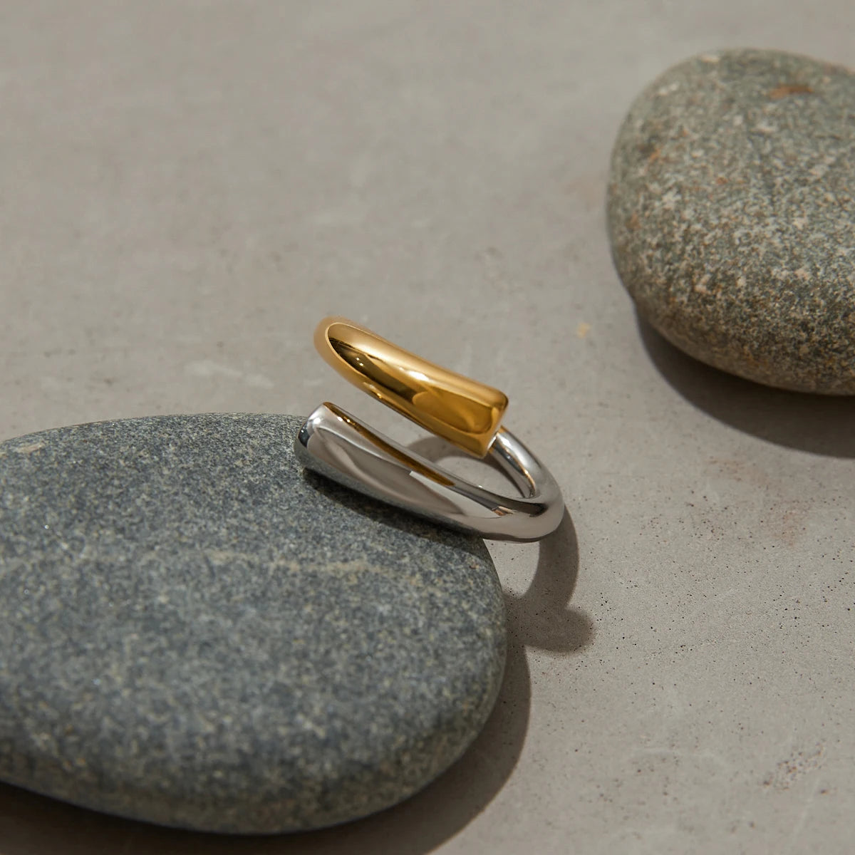 Stainless steel line ring with gold and silver tones displayed on smooth gray stones