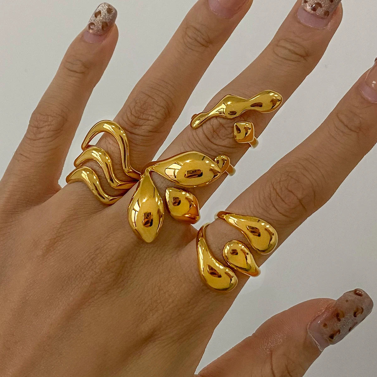 Hand wearing unique statement gold rings with organic fluid shapes on multiple fingers