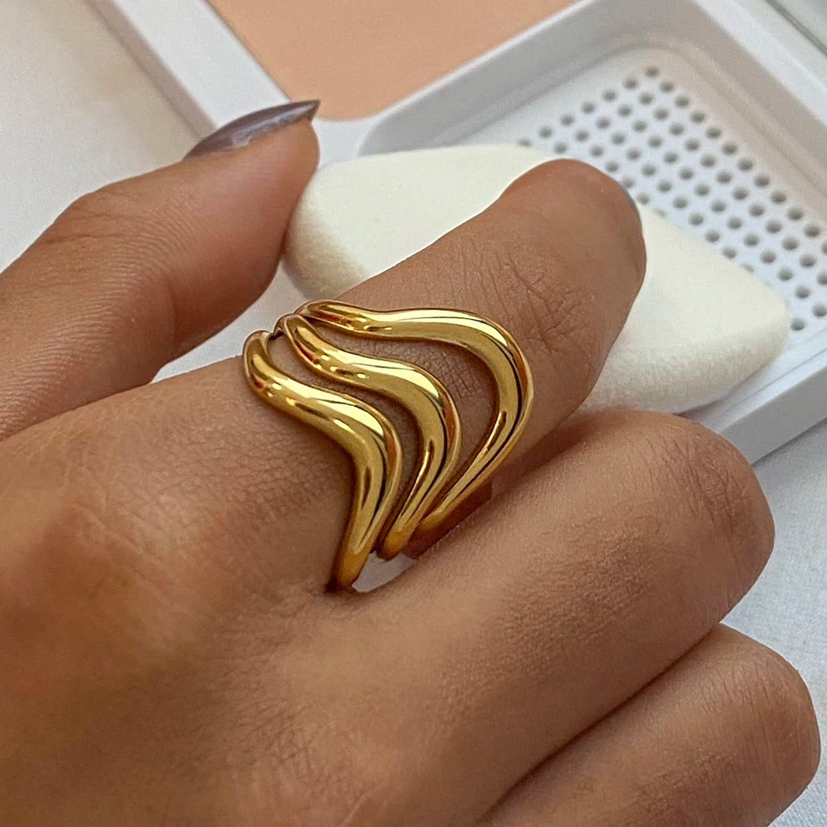 Hand wearing stylish statement gold rings with a wavy design in a close-up view