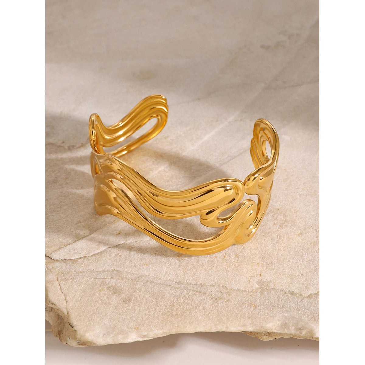 Unique gold bangle with fluid wavy design on a textured stone surface