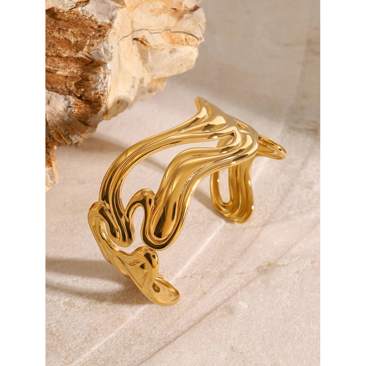 Unique gold bangle with a modern wavy design displayed on a beige stone surface