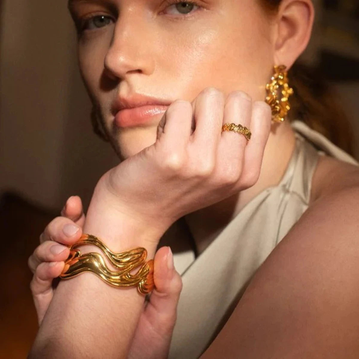 Woman wearing a unique gold bangle bracelet and matching gold earrings showcasing elegant jewelry