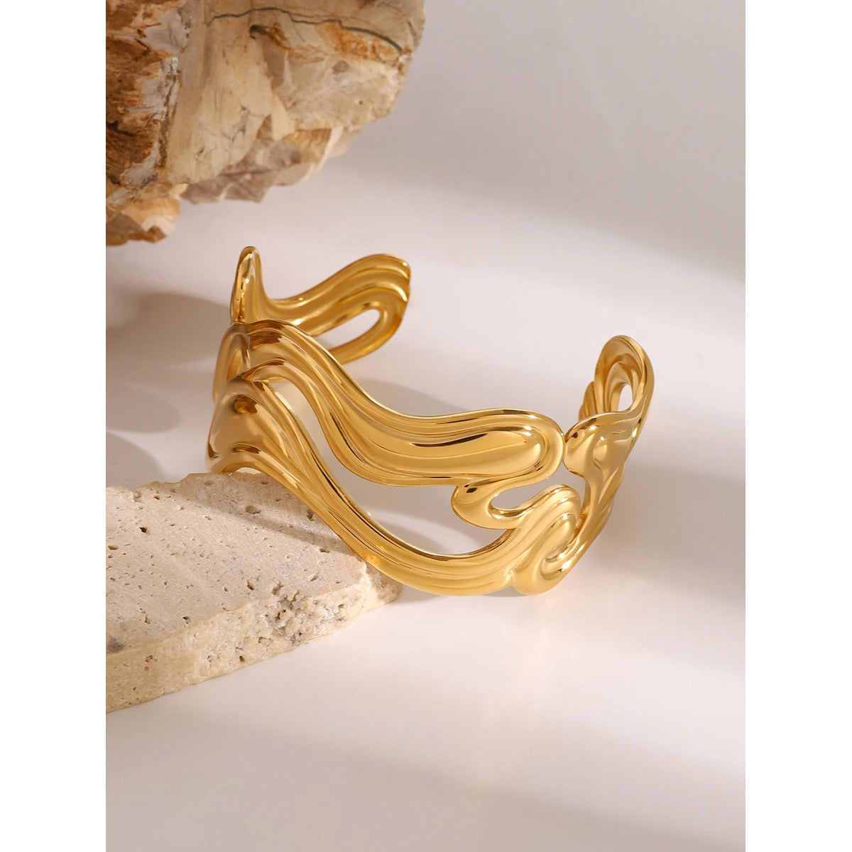 Unique gold bangle with elegant wavy design displayed on natural stone surface