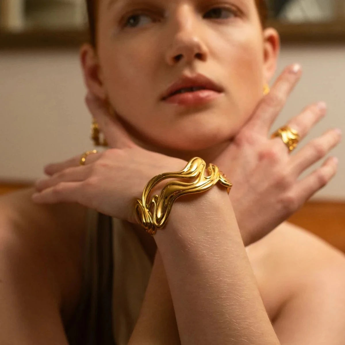 Unique gold bangle with wavy design worn by a woman showcasing elegant and artistic jewelry style