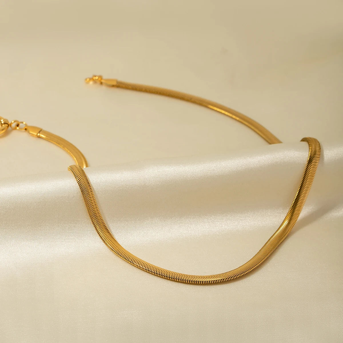 Bold gold statement necklace with smooth curved design displayed on a beige fabric background