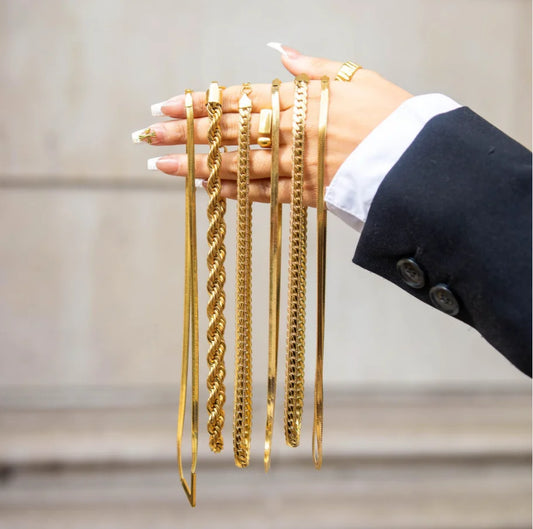 Hand holding multiple bold gold statement necklace chains with various link styles