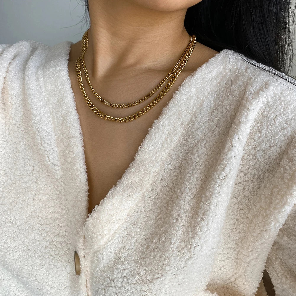 Woman wearing a bold gold statement necklace with layered chains over a white textured top