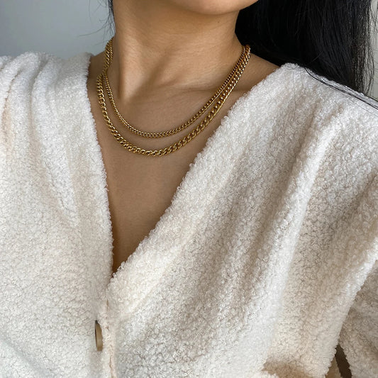 Woman wearing a bold gold statement necklace with layered chains over a white textured top