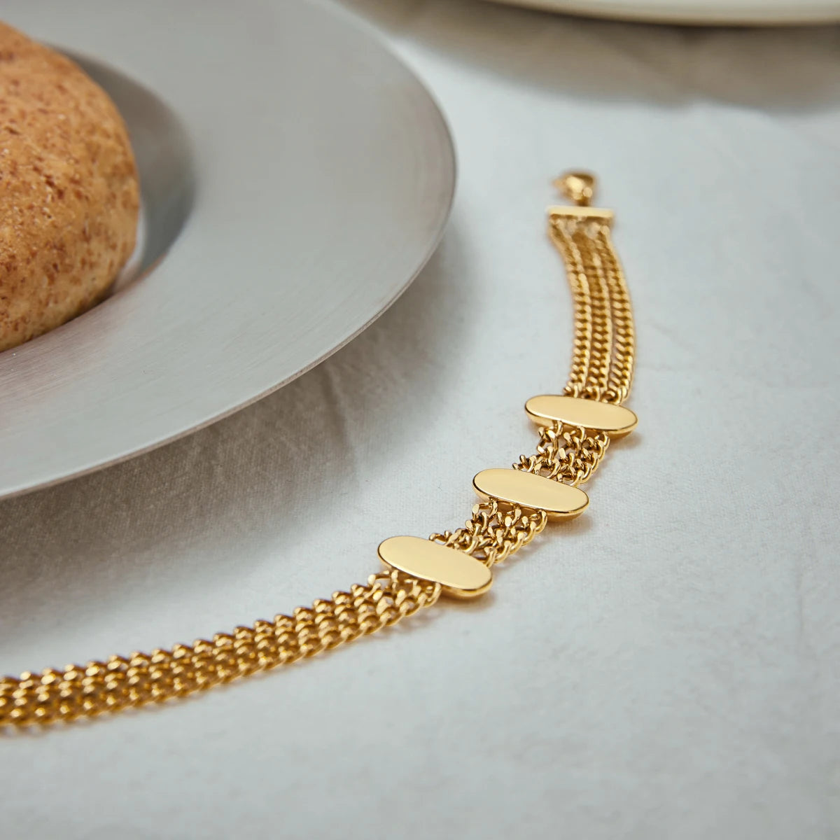 Fashionable gold bracelet with multiple chain links and smooth oval accents displayed near a plate