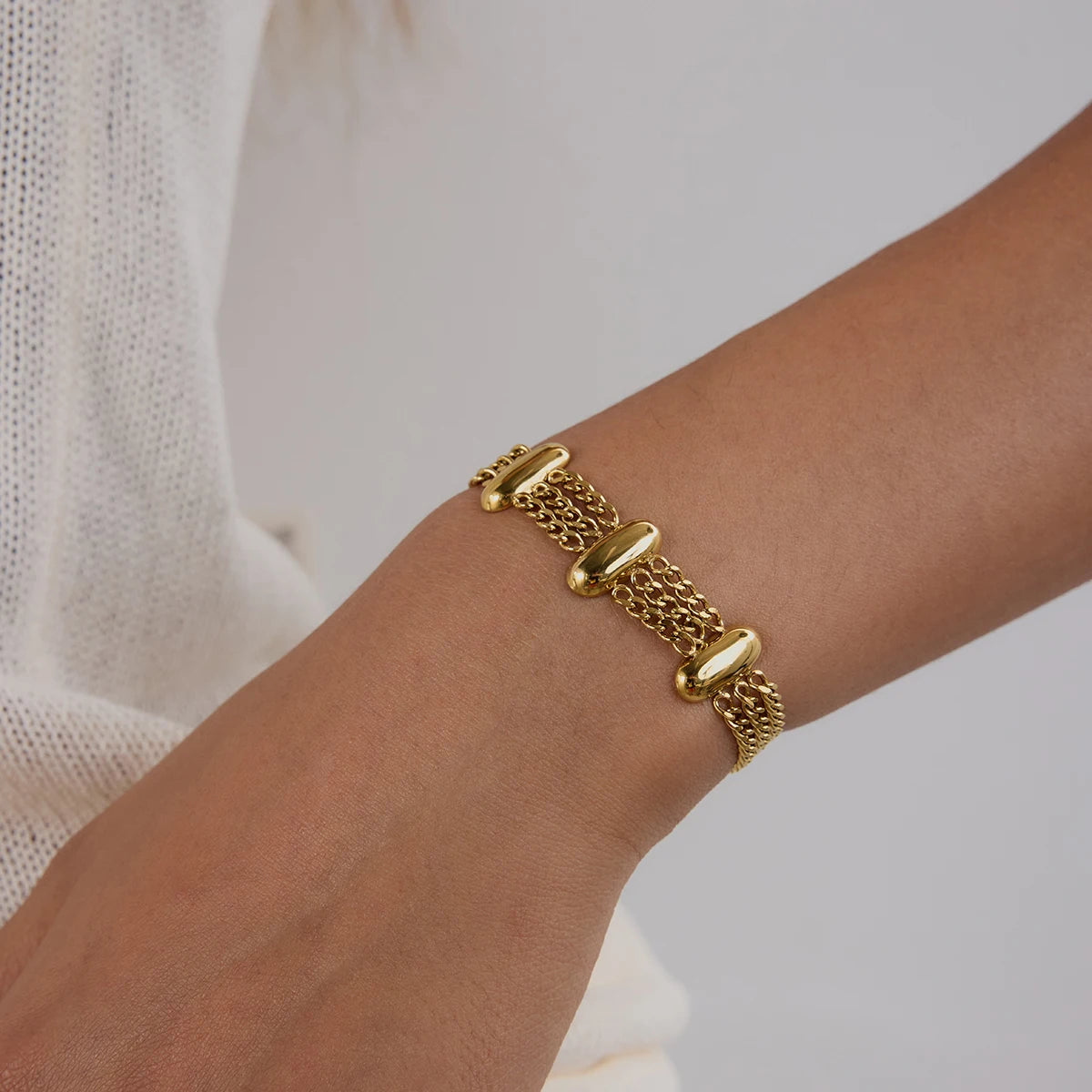 Fashionable gold bracelet on wrist featuring multiple chain strands and polished oval accents