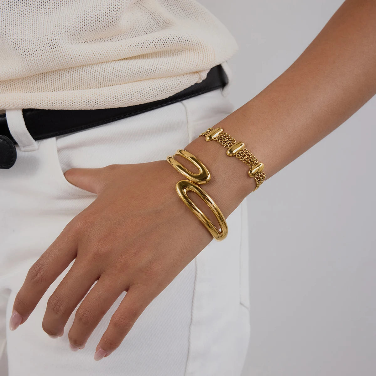 Fashionable gold bracelet on wrist with textured links and modern design on model wearing white pants