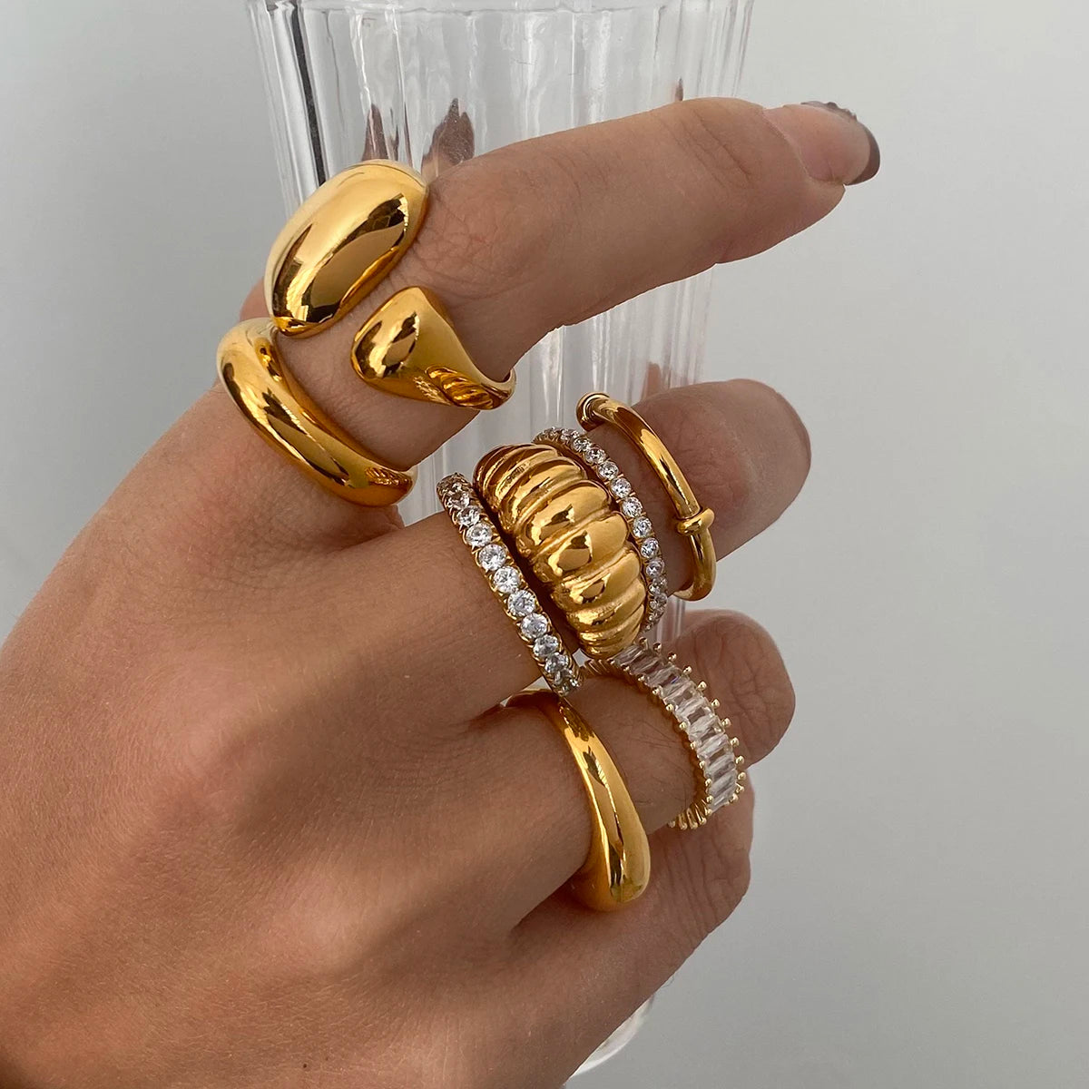 Fashionable stackable rings in gold and silver with gemstones worn on hand holding a glass