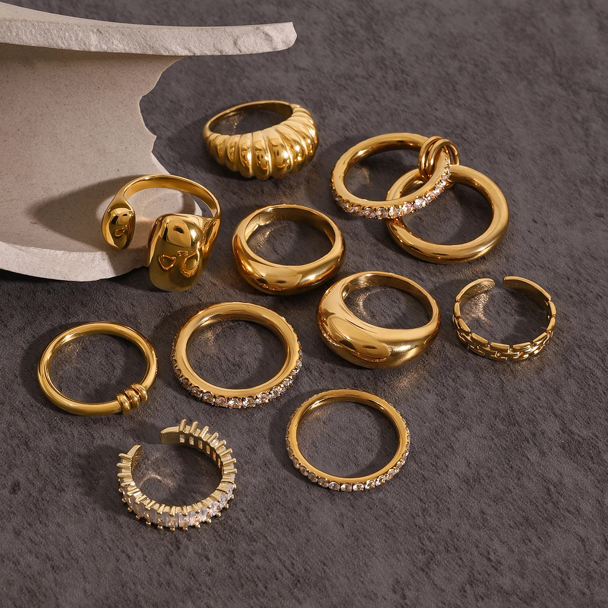 Set of Fashionable Stackable Rings in gold with various designs and sparkling accents on gray surface