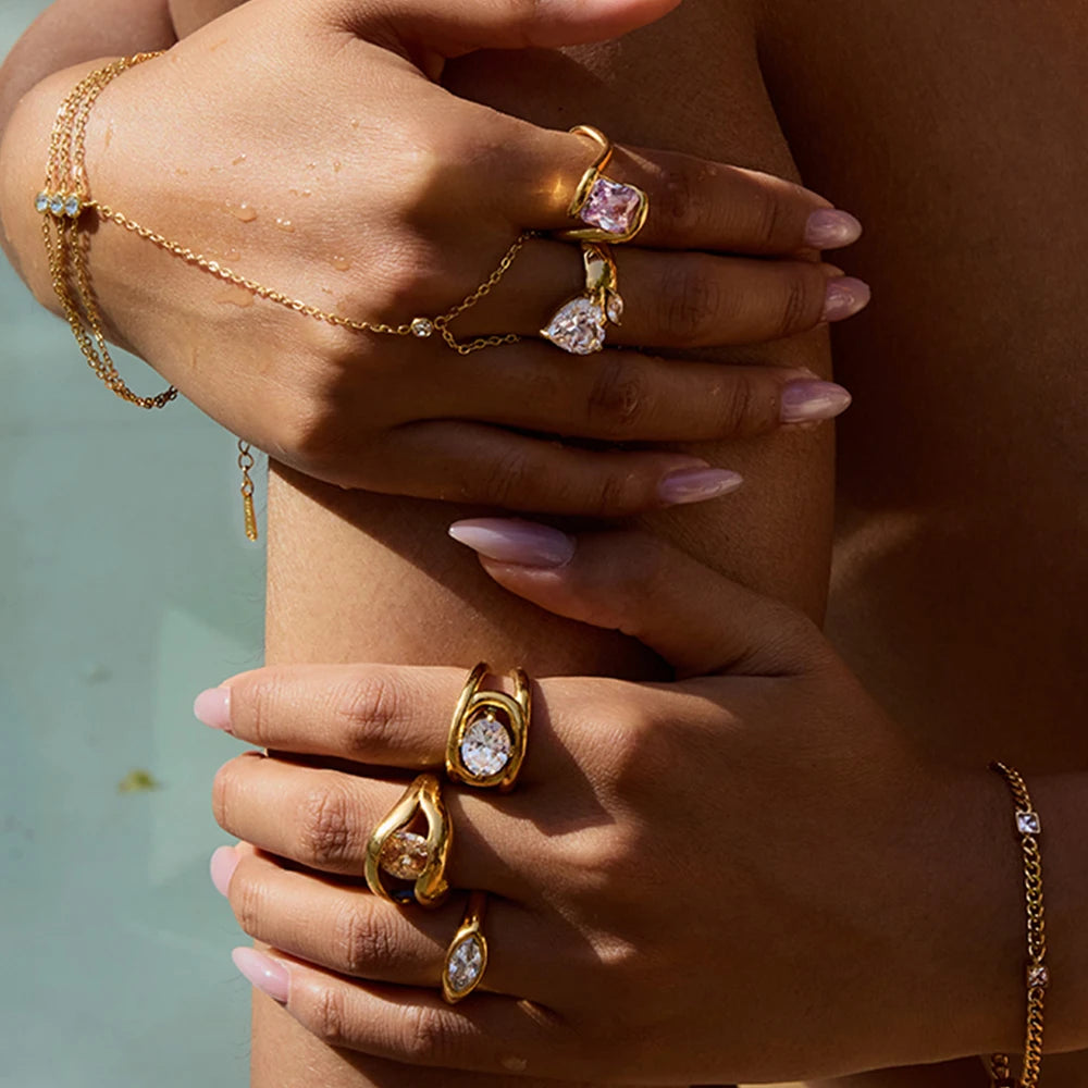 Close-up of hands wearing multiple gold rings including a geometric statement ring with clear gemstones