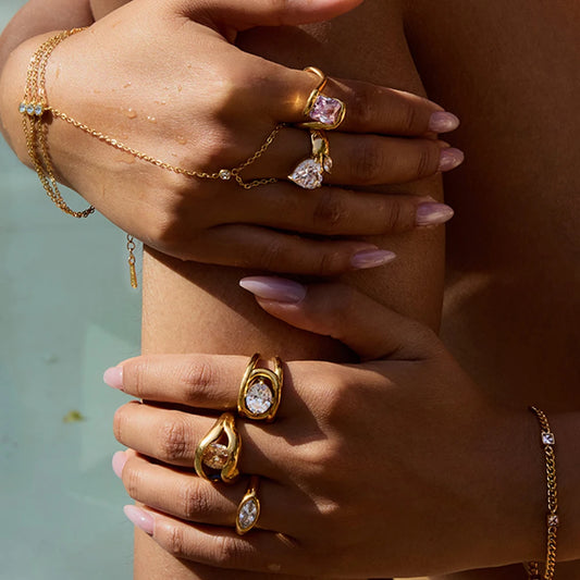 Close-up of hands wearing multiple gold rings including a geometric statement ring with clear gemstones