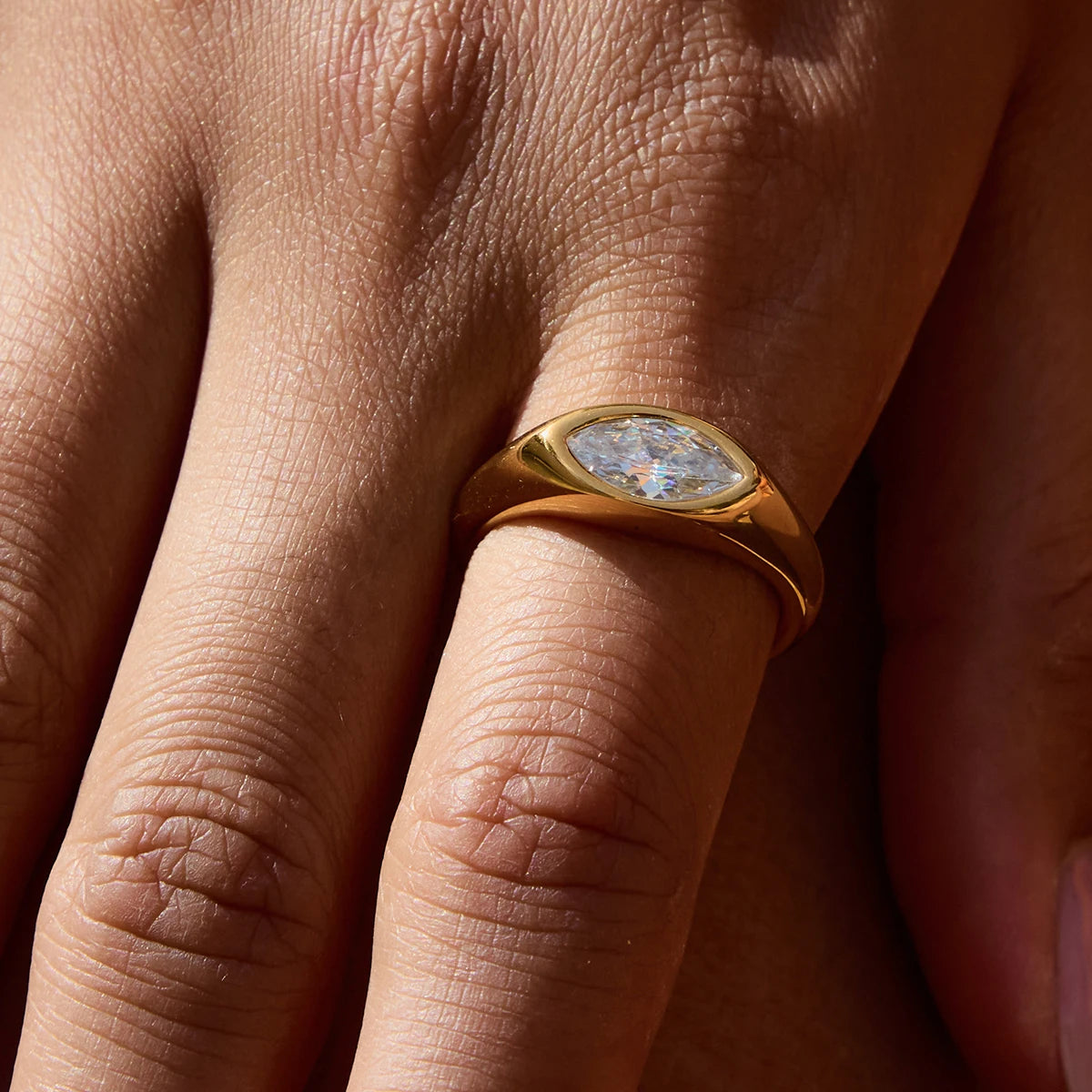 Gold geometric statement ring with a marquise-cut clear stone worn on finger