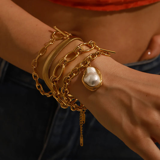 Elegant gold stacked chain bracelet featuring a large pearl charm worn on wrist