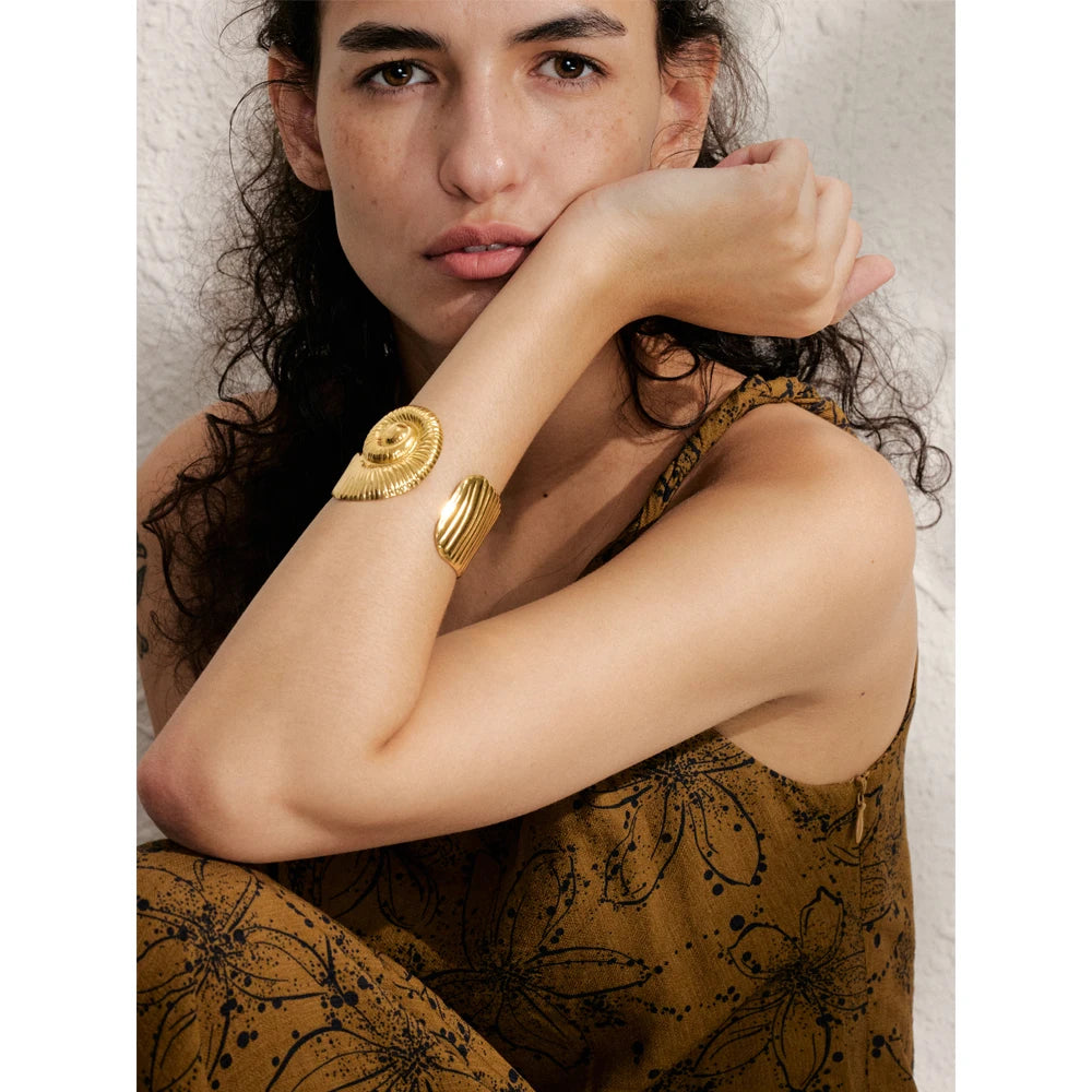 Woman wearing a gold waterproof open bangle on her forearm with a patterned brown sleeveless dress