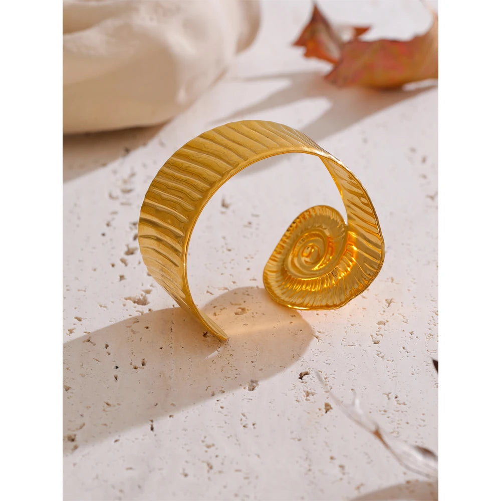 Gold textured waterproof open bangle with spiral design resting on stone surface